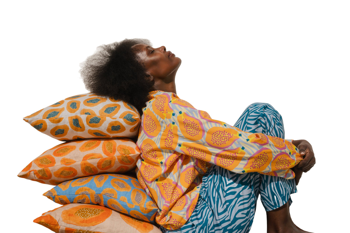 Model seated against a stack of yellow, orange and blue printed COCOLILI cushions