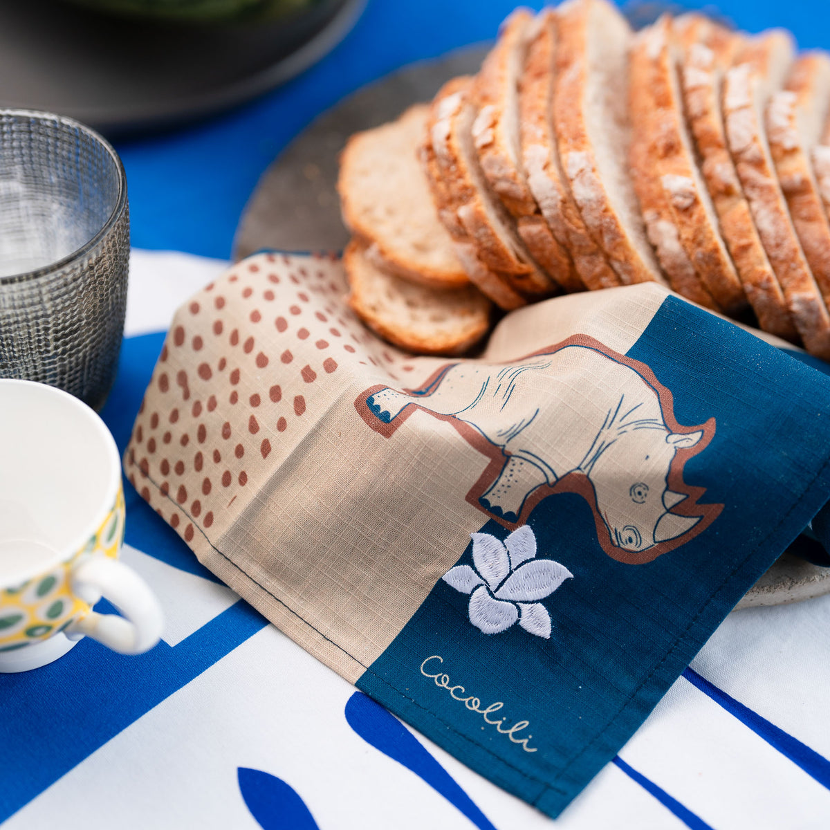 COCOLILI rhino napkin beside fresh bread on a blue and white table