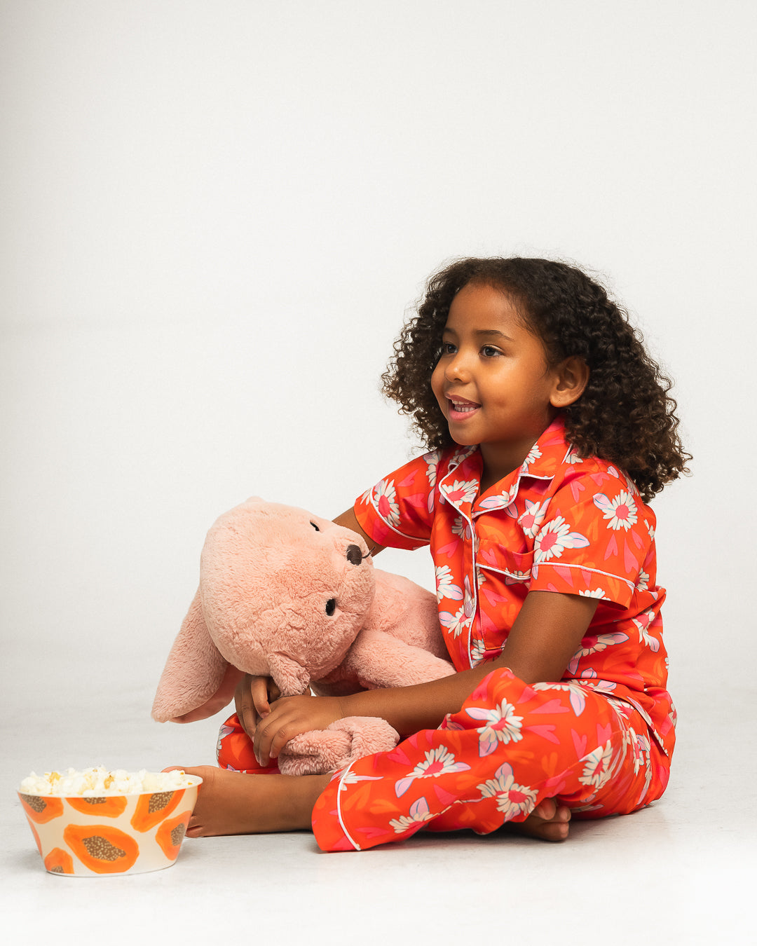 Child in a red floral COCOLILI outfit with a pink elephant soft toy