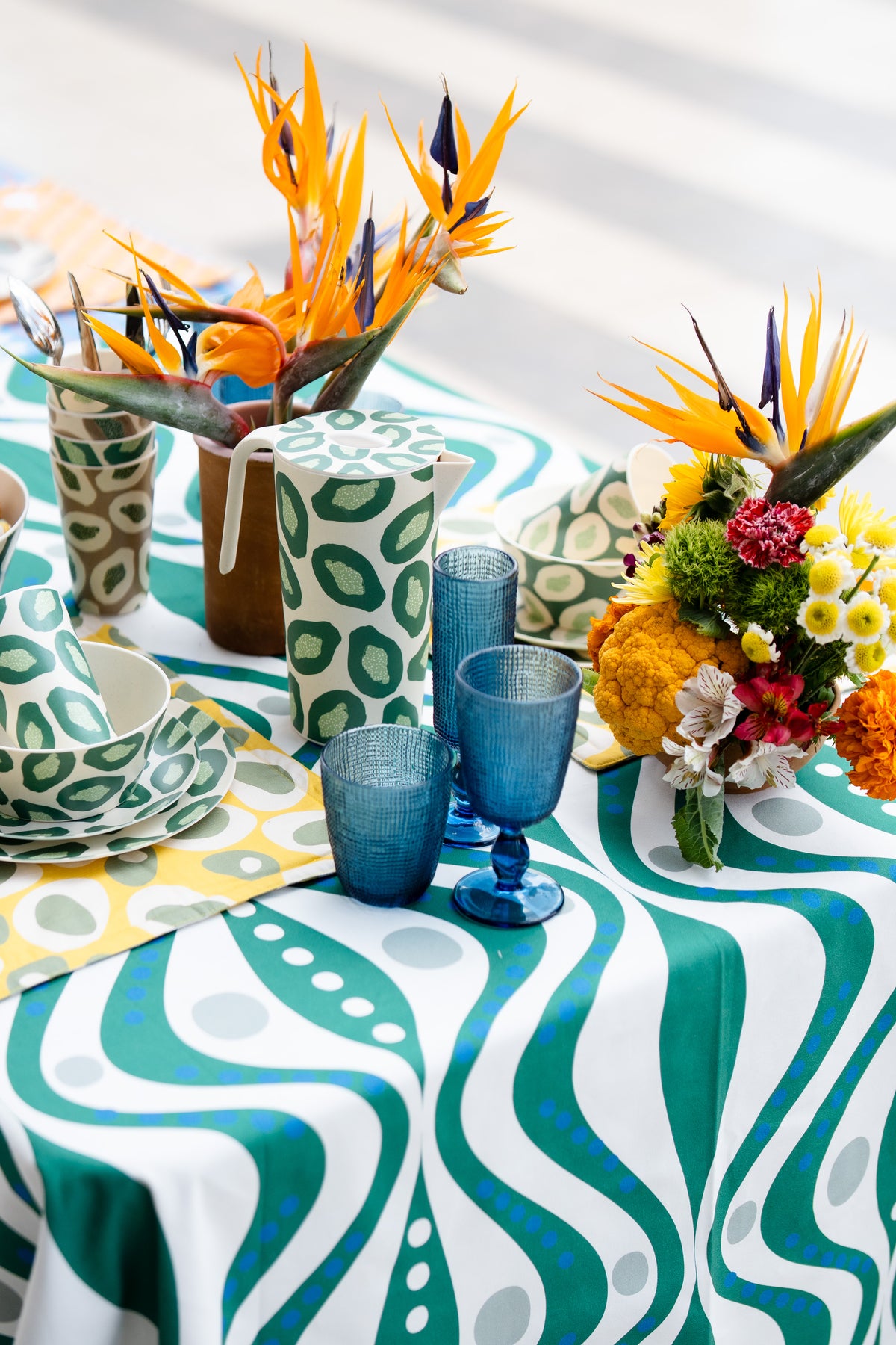Green and white COCOLILI table setting with printed dinnerware, blue glasses and fresh flowers